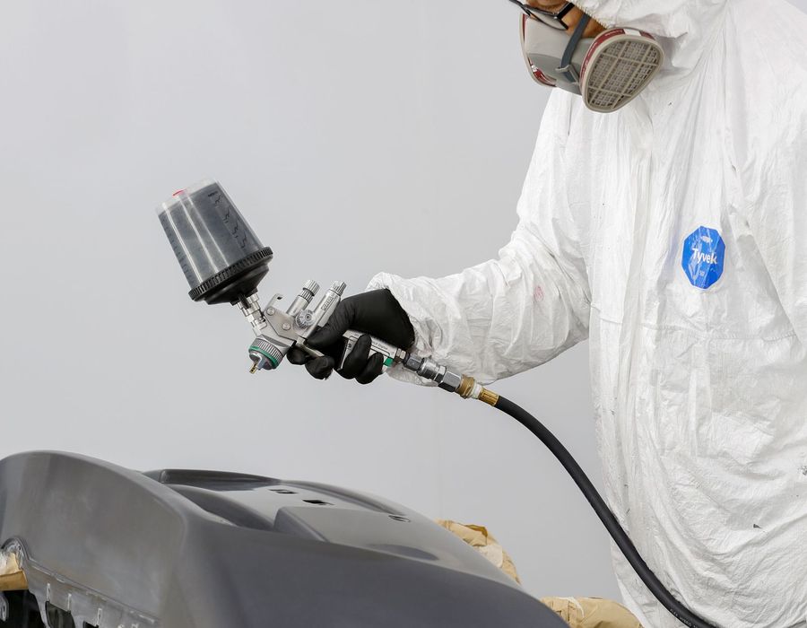 Technician in protective gear spray painting a car bumper