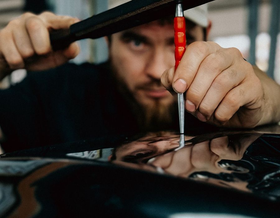 Technician performing paintless dent repair on a dark car panel