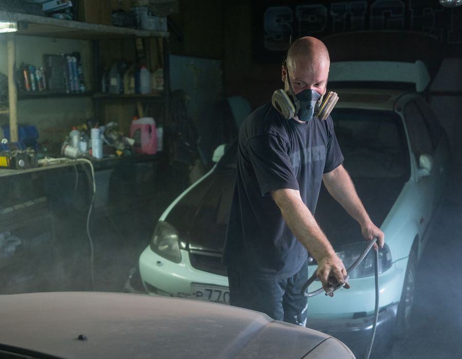 Technician spray painting a car in a workshop booth
